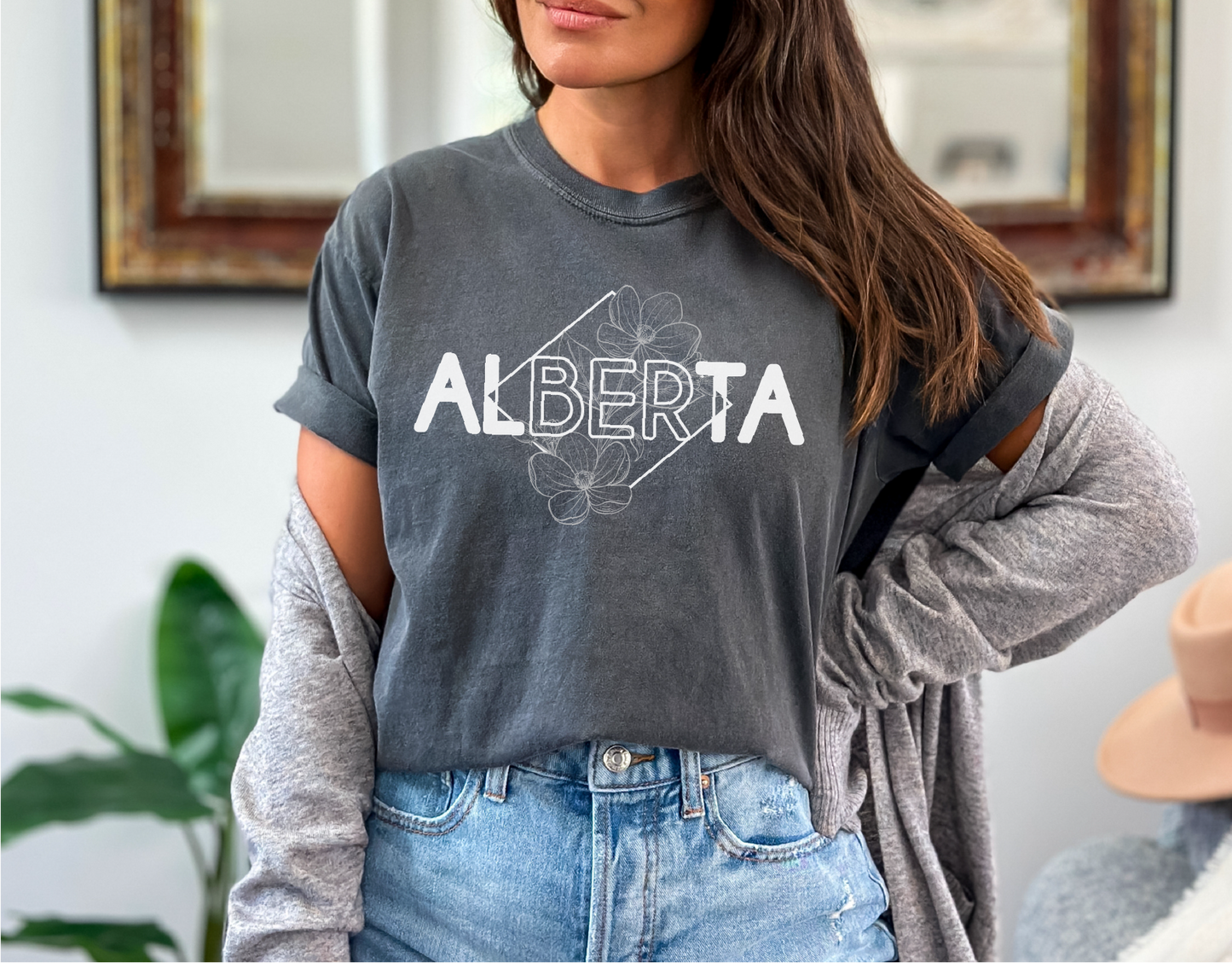 Person wearing a gray 'Alberta' t-shirt with floral design indoors.