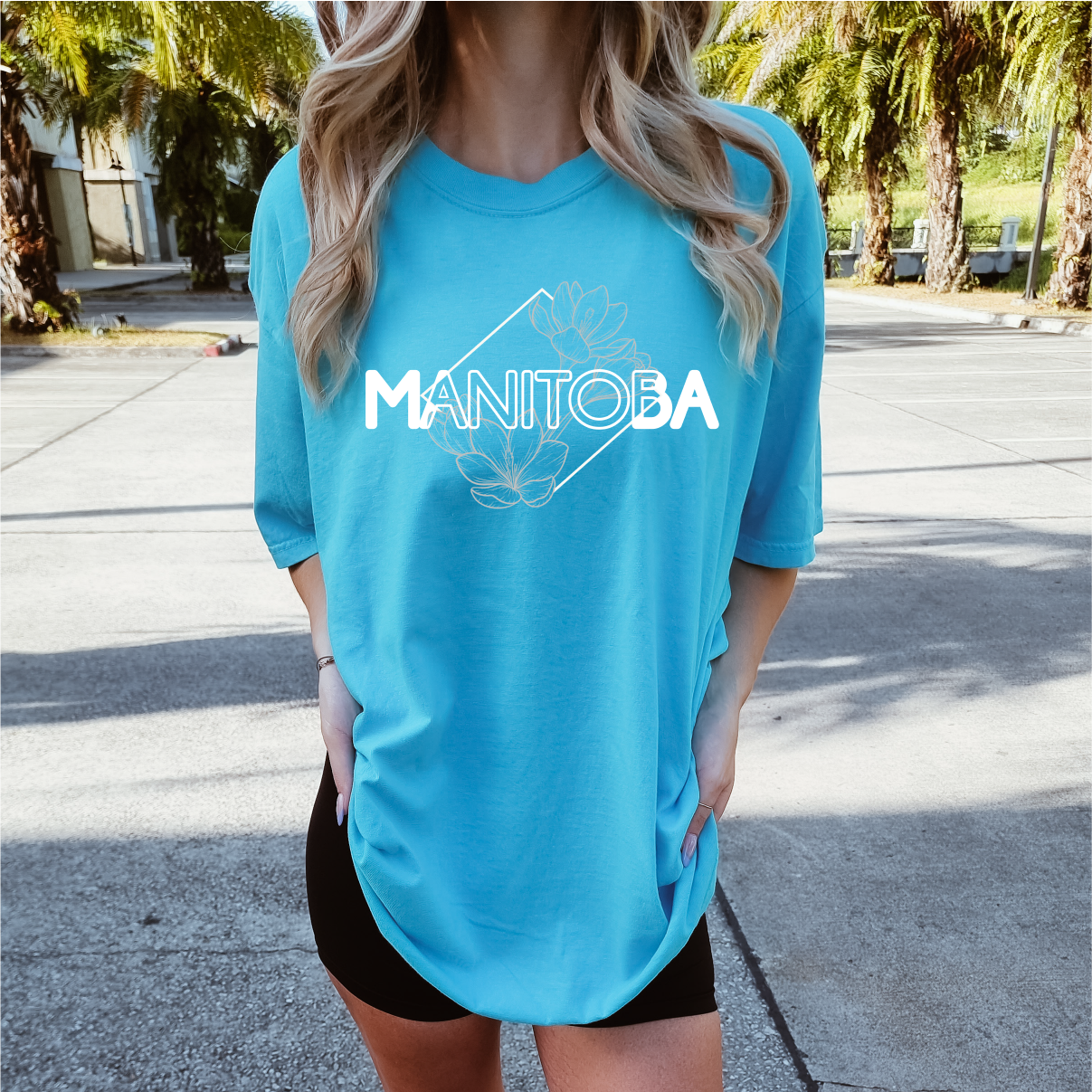 Person wearing a blue t-shirt with 'Manitoba' printed on it, standing outdoors.